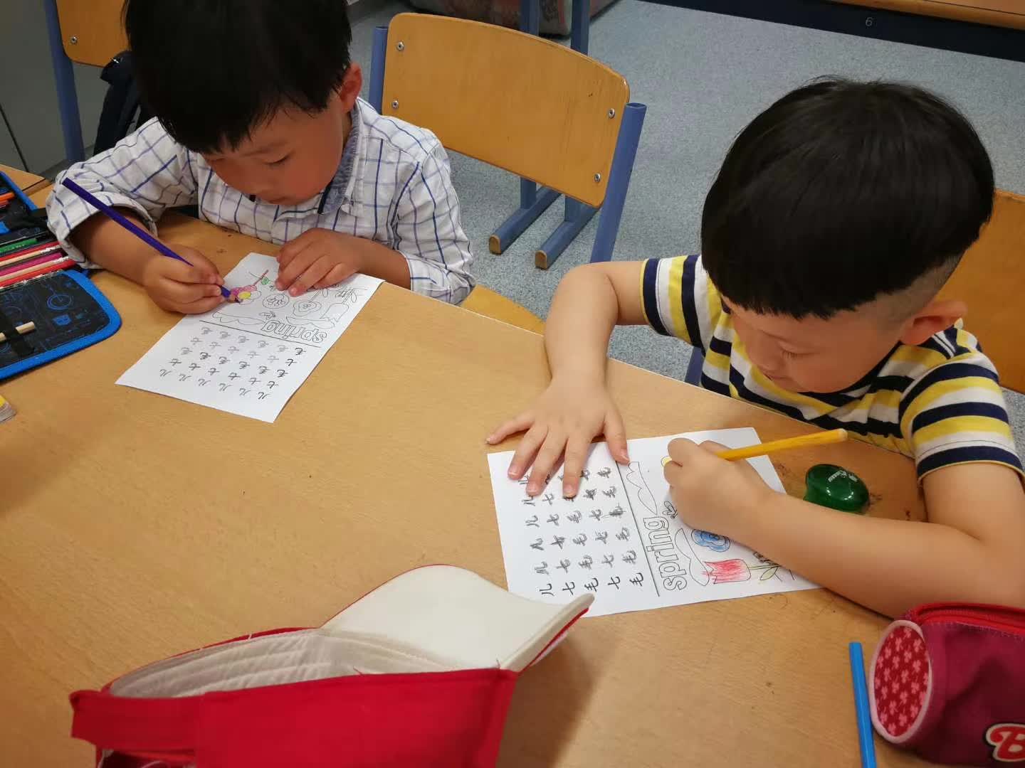 Zwei Kinder schreiben konzentriert chinesische Arbeitsblätter.